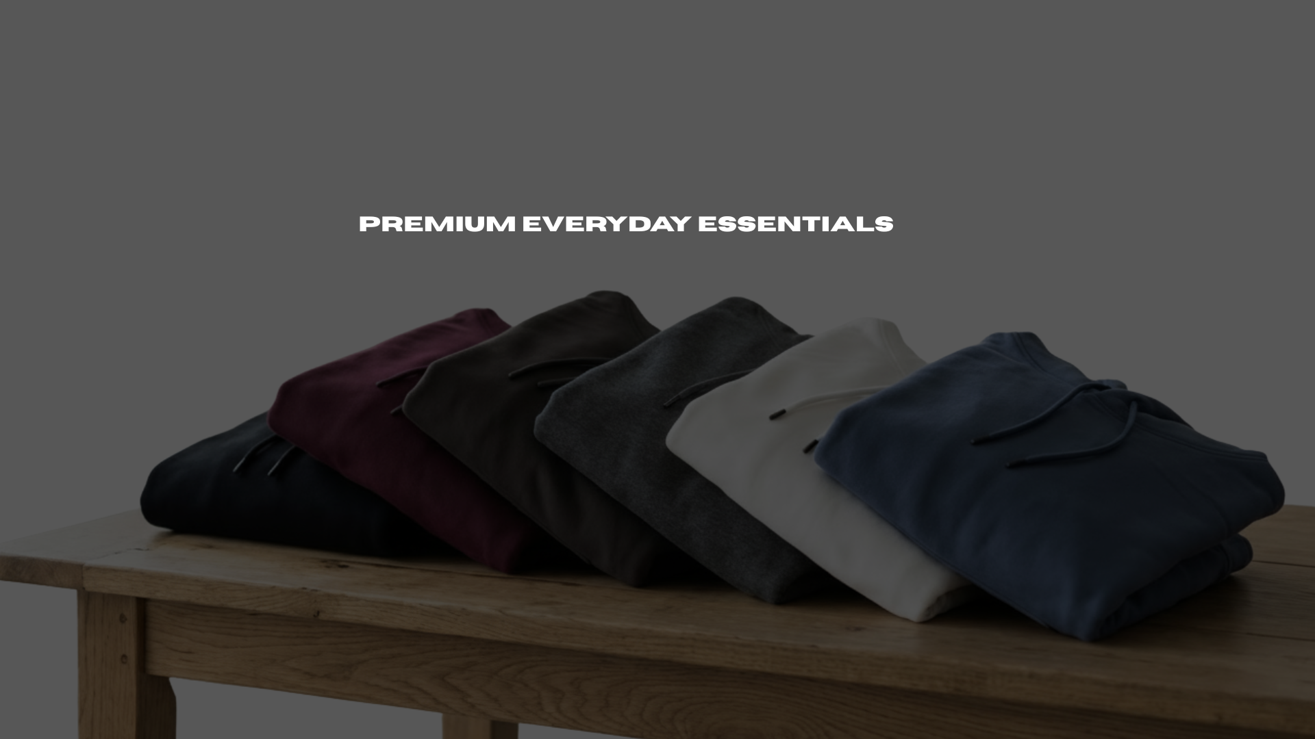 Folded hOODIES in various colors on a wooden table with 'Premium Everyday Essentials' text.